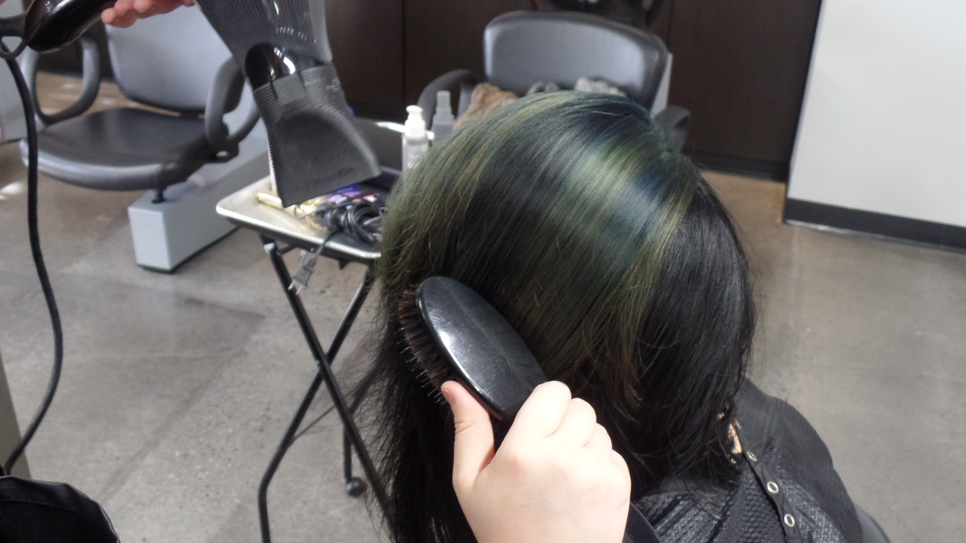 Student putting the finishing touches on a model's green-highlighted hair.