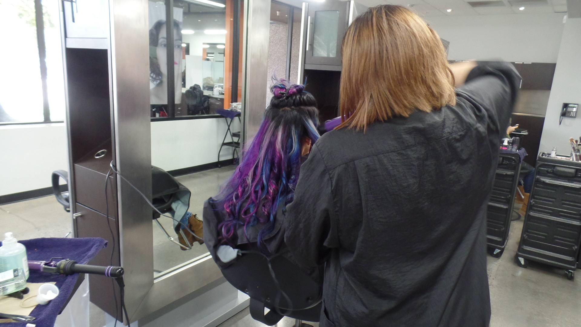 Student styling a model's long black, purple and pink hair.