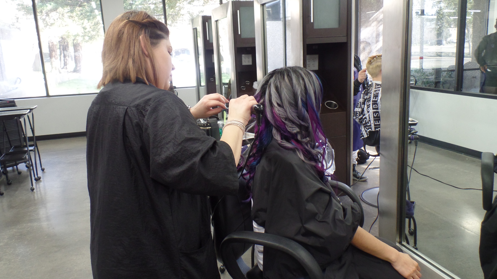 Student styling a model's black, pink and purple hair.