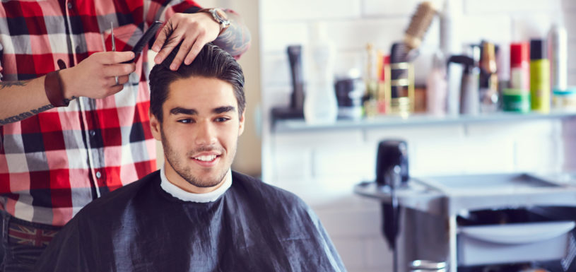 A young man sits and gets a haircut in a salon. 